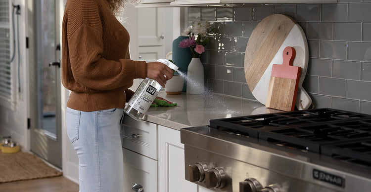 A woman is spraying a kitchen with a Better Life sprayer.