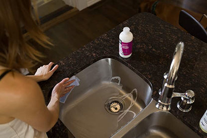 A woman cleaning a kitchen sink with Clean Happens Kitchen & Bath Scrubber.